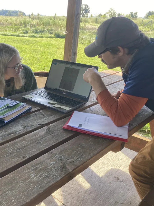 photo of 3 people sitting at a picnic table looking at a laptop screen
