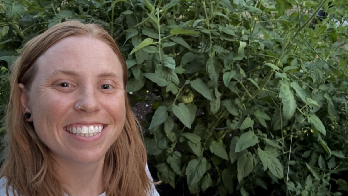 Red haired girl standing in front of tomato plants. 