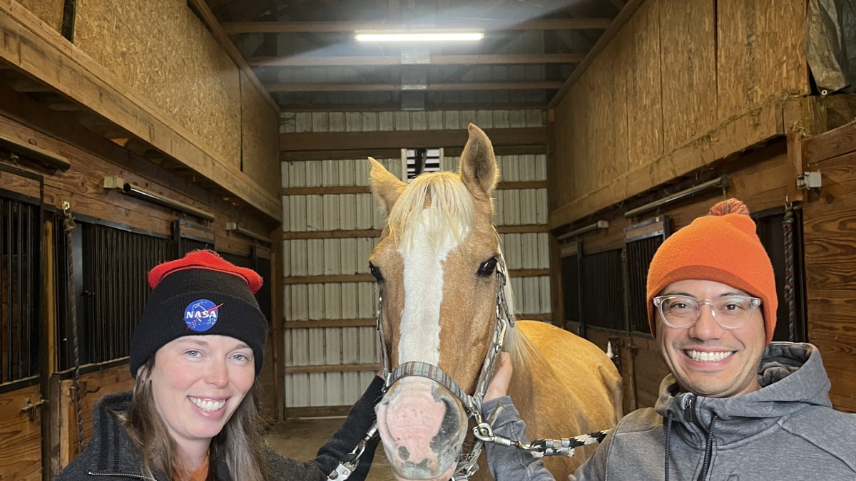 Rob and Erika taking a picture next to a horse in a barn.