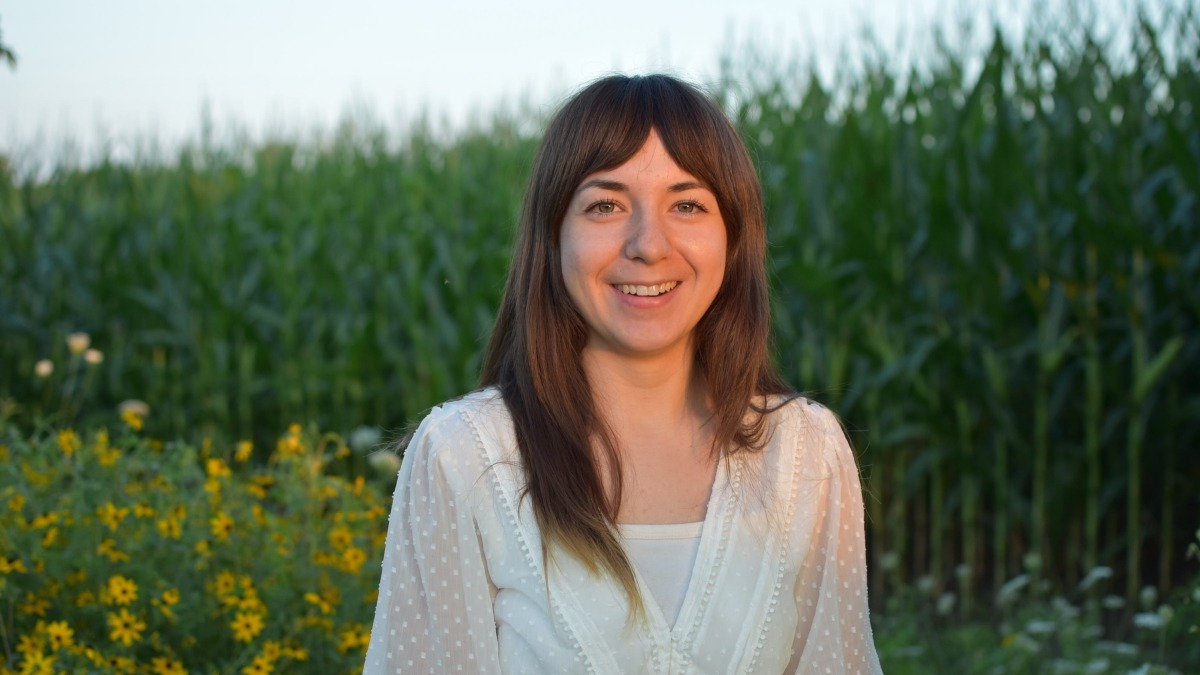 Female standing in front of corn field and pollinator habitat.