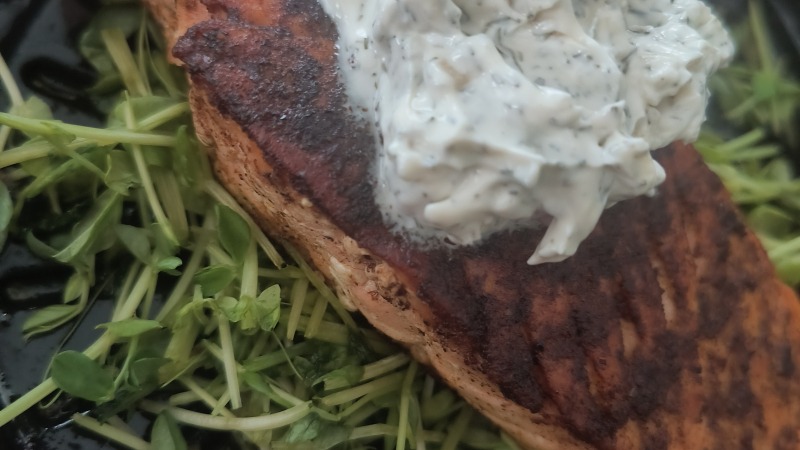 Salmon filet over sauteed pea shoots with dill cream garnish 