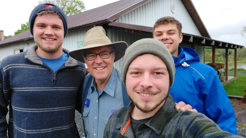 A family of three looking at the camera which is pointed up from the ground with a young woman on the left, a young man in the middle, and a boy toddler on the right all smiling