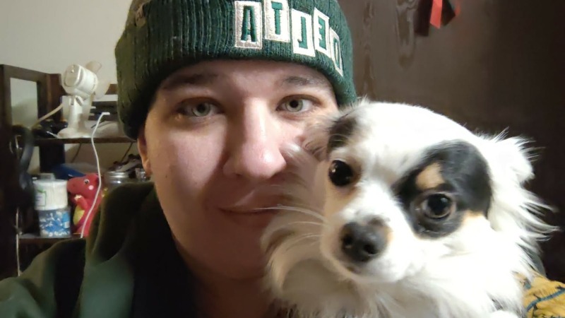 Owner wearing green delta hat and shirt holding black and white pappillon puppy