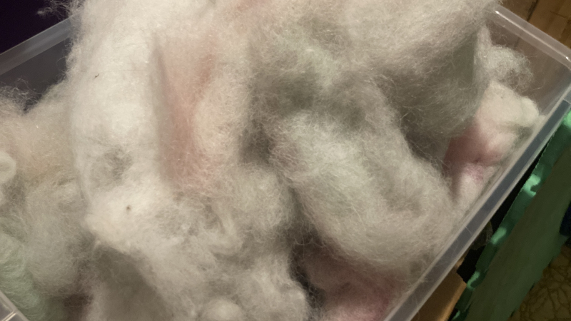 A bucket full of various light colored natural fibers that look like a multicolored cloud