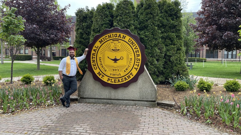 A man after his graduation ceremony in front of a university sign 