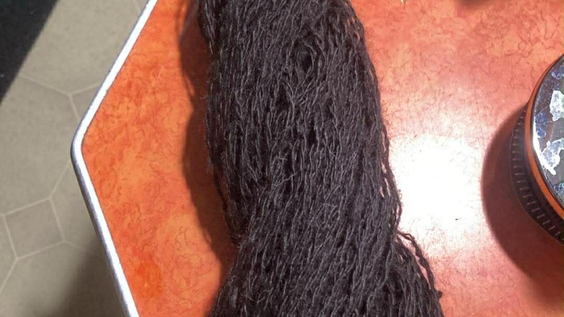 Black alpaca fiber spun and twisted into a completed skein on an orange counter