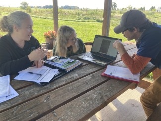 photo of 3 people sitting at a picnic table looking at a laptop screen